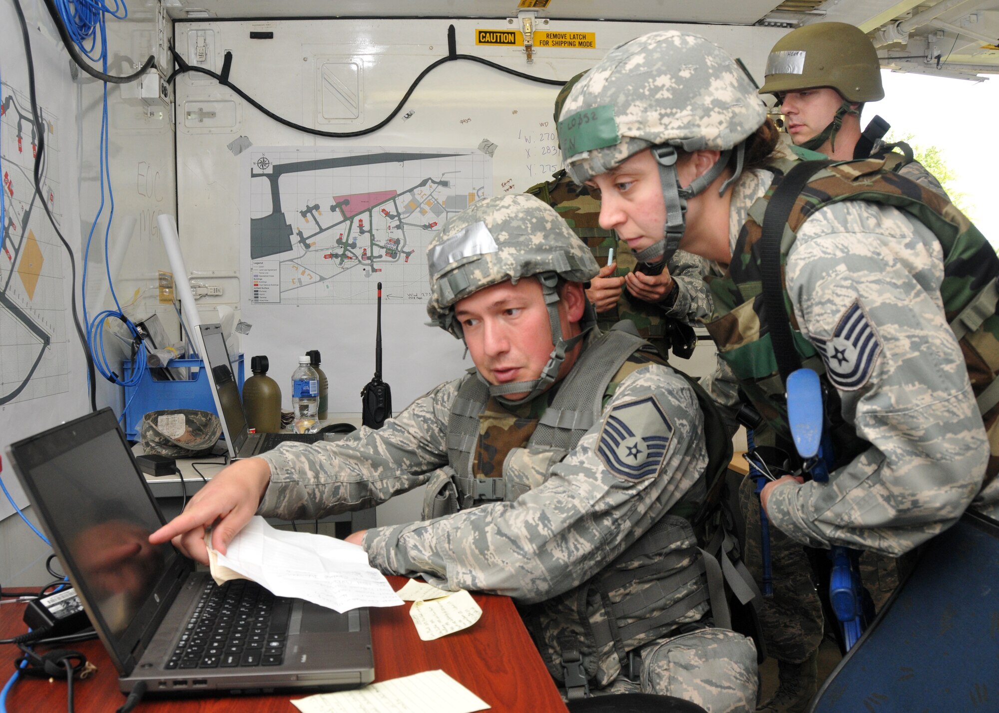 An Airman from the 104th Emergency Management Flight, 104th Fighter Wing, Barnes Air National Guard Base, Westfield, Mass., looks over the shoulder of another EM guardsman as they discuss details for a situation report during a Silver Flag exercise May 16, 2015, Ramstein Air Base, Germany. Silver Flag is an eight-day training course designed to prepare Airmen for any bare-base deployment. (U.S. Air National Guard photo by 2nd Lt. Bonnie Harper)