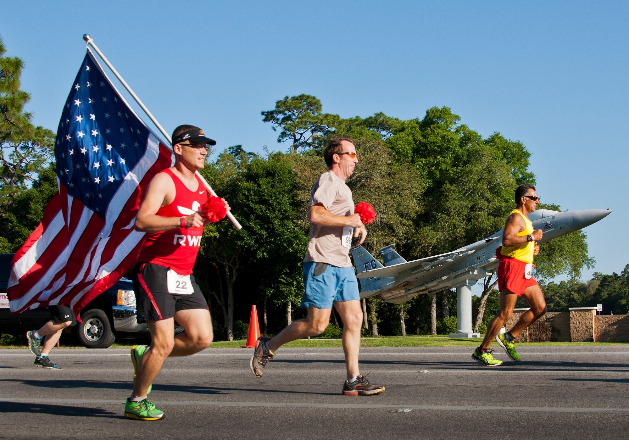 Runners carry flags and carnations as they pass the 33rd Fighter Wing F-15 static display at the 30th Anniversary Memorial Gate to Gate run May 23 at Eglin Air Force Base, Fla.  More than 1,500 participated in this year’s event.  (U.S. Air Force photo/Samuel King Jr.)