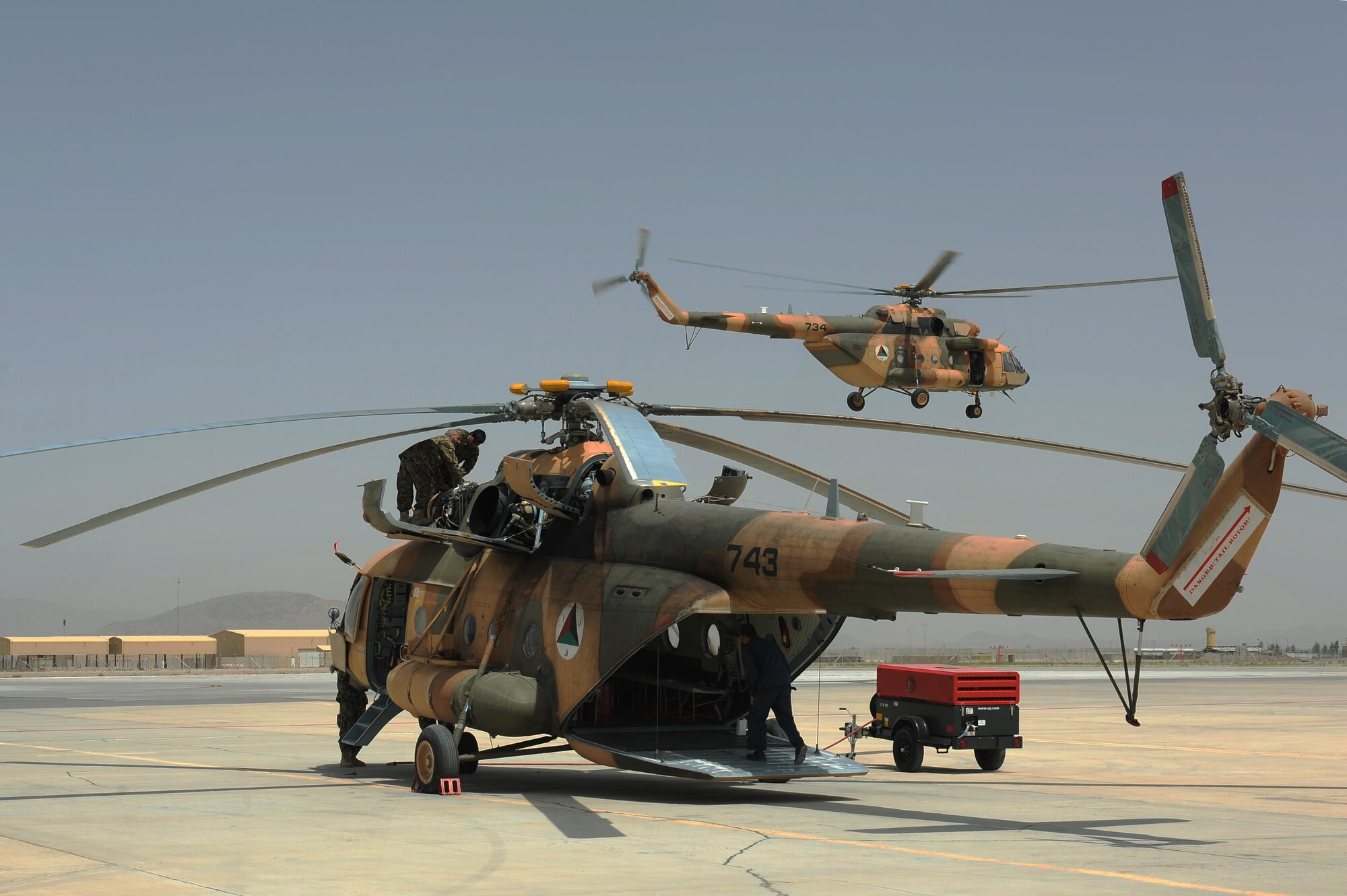 Afghan Air Force maintainers work to fix an Mi-17 at Kandahar Air Wing while another Mi-17 flies off to perform a mission, April 29, 2015. (U.S. Air Force photo/Capt. Jeff M. Nagan)