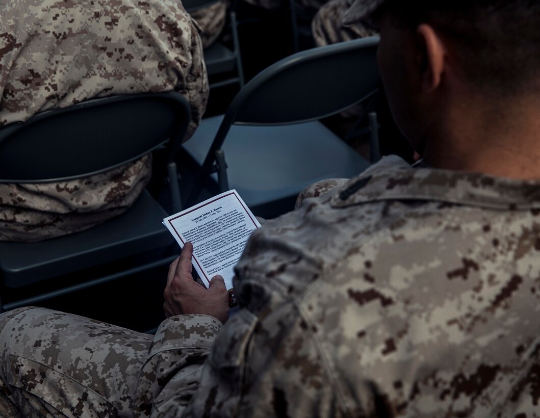 U.S. Marine Master Sgt. Sascha Fischer with the 15th Marine Expeditionary Unit takes a moment to read a pamphlet during the memorial of Cpl. Joshua Barron and Lance Cpl. Matthew Determan aboard the flight deck of the USS Essex (LHD 2) at sea in the Pacific Ocean, May 23, 2015. Marines and Sailors with the 15th MEU and the Essex Amphibious Ready Group paused during deployment to pay their respects and honor the two Marines. (U.S. Marine Corps photo by Cpl. Elize McKelvey/Released)