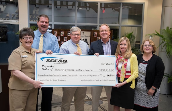 Navy Capt. Amy Burin, commanding officer of Space and Naval Warfare (SPAWAR) Systems Center (SSC) Atlantic, along with Executive Director Steve Dunn, Facilities Manager Darrell Denaux and Energy Program Manager Tom Egbert accept a rebate check from South Carolina Electric and Gas (SCE&G) in the amount of $797,215 May 26 at the Naval Weapons Station - Joint Base Charleston. The check is a result of successful energy savings rebate initiatives under SSC Atlantic’s Energy Savings Performance Contract (ESPC)through Huntsville Center and SCE&G’s EnergyWise for your Business program. 