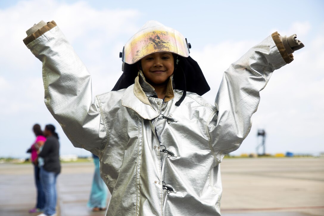 A student from E.C. Killin Elementary School, Camp Foster, Okinawa, Japan, poses for a picture while wearing thermal protective equipment, May 8, during a tour of the aircraft rescue and fire fighting station on Marine Corps Air Station Futenma, Okinawa, Japan. The tour provided students with the understanding of ARFF Marines’ responsibilities within Headquarters and Headquarters Squadron, MCAS Futenma and the opportunity to explore various career paths. During the visit, ARFF Marines demonstrated the use of hand lines, also known as fire hoses; mounted water turrets; and the proper use of various personal protective equipment, such as gas masks, helmets with face shields, proximity equipment and footwear. After the demonstrations, the Marines taught the students how to properly use and operate the equipment. (Marine Corps Photo by Cpl. Janessa K. Pon/ Released)