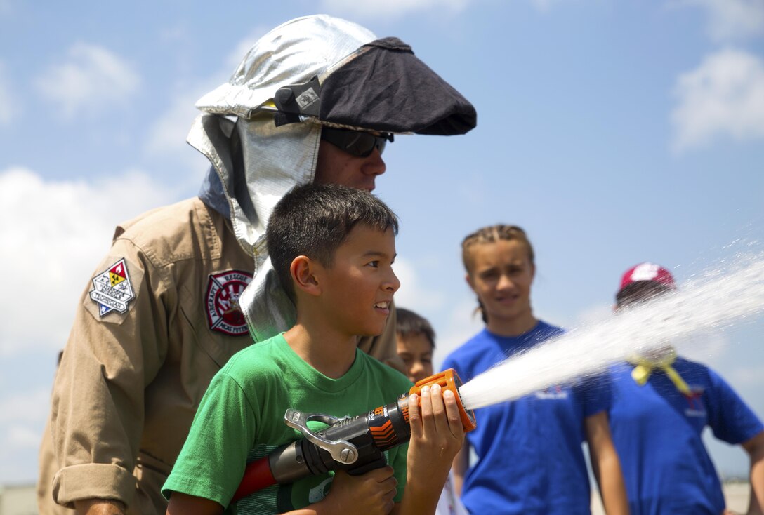 Lance Cpl. Conner M. Levinsky assists a student from E.C. Killin Elementary School, located on Camp Foster, Okinawa, Japan, in operating a hand line, also known as a fire hose, May 8, during a tour of the aircraft rescue and fire fighting station on Marine Corps Air Station Futenma, Okinawa, Japan. The tour was a part of a visit to the flight line on MCAS Futenma that provided students with the understanding of the ARFF Marines’ responsibilities with Headquarters and Headquarters Squadron, MCAS Futenma and the opportunity to explore various career paths. Levinsky, a rescueman with ARFF, H&HS, MCAS Futenma, is an El Dorado Hills, California, native. (Marine Corps Photo by Cpl. Janessa K. Pon/ Released) 