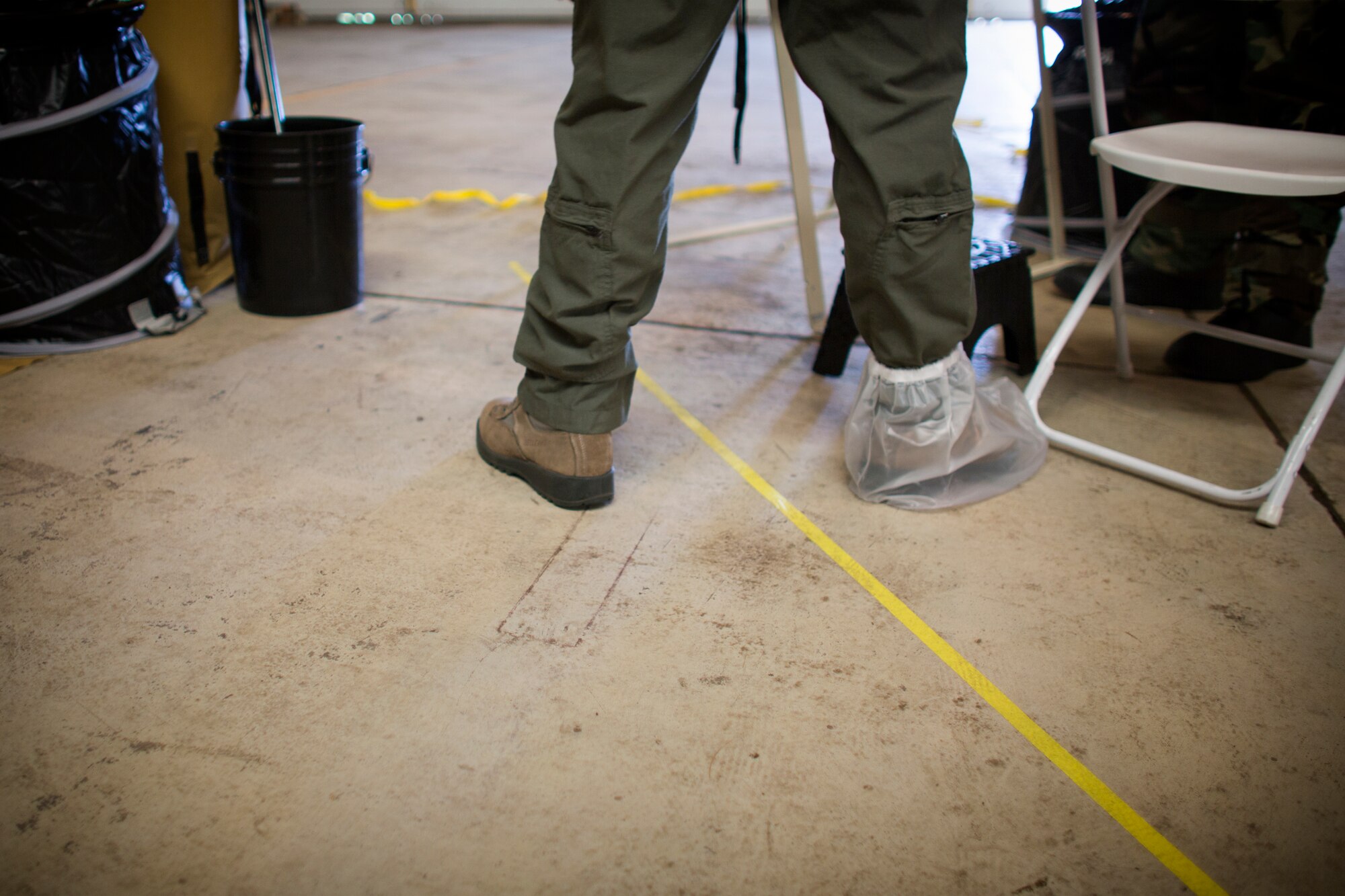 An aircrew member from the 36th Airlift Squadron passes one foot over the delineation line separating the contact hazard area from the vapor hazard area through during a Samurai Readiness Inspection at Yokota Air Base, Japan, May 20, 2015. Airmen from the 36th AS and 374th Operations Support Squadron performed aircrew decontamination procedures with the Lightweight Inflatable Decontamination System (LIDS). The LIDS takes about 20 minutes to set up and consists of four stations for rinsing off excess chemicals and a process to dispose of contaminated clothing and aircrew equipment. (U.S. Air Force photo by Osakabe Yasuo/Released)
