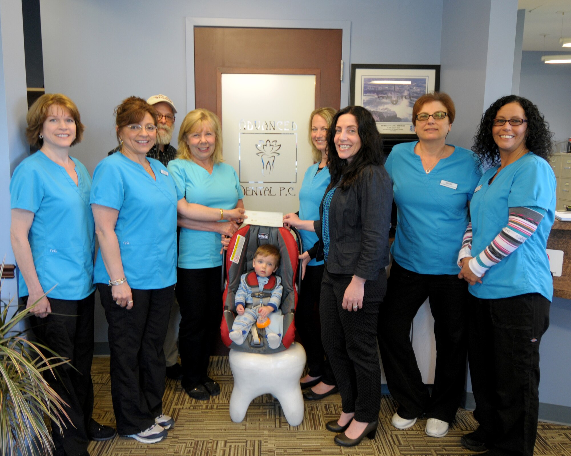 Ms. Mary Grace Scarpelli (second from left), Operation Whiter-Brighter Coordinator from Advanced Dental presents a check for $3,600 to Captain Gina Pizziconi Cupples (third from right), President of Friends of Family Support Association, Niagara Falls Air Reserve Station at the Advanced Dental office in Niagara Falls, N.Y. on May 20, 2015. Looking on are (left to right) Ms. Carla Siwinski, dental assistant, Dr. Stuart J. Weinstein, dentist/owner, Ms. Luann Pelletier dental assistant, Chance Cupples, (future patient?), Ms. Wendy Mariano, dental assistant, Ms. Susan Yuroshoski, supervising assistant, and Ms. Cindy Garner, dental assistant.  The program now in its ninth year at Advanced Dental of Niagara Falls, New York offers professional whitening at a greatly reduced cost to all patients.  100% of all proceeds from the program are donated to the Base Family Readiness Center. The money will be used for various programs to benefit local military members and their families. (U.S. Air Force photo by Peter Borys)