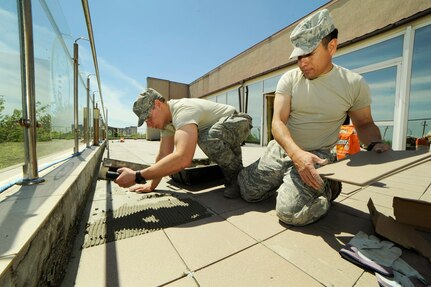 Oregon Air National Guard Tech Sgt. Ramon Lopez, right, and Staff Sgt. Jared Levitt, assigned to the 142nd Fighter Wing Civil Engineer Squadron, work together to size and place new exterior tile flooring to a medical facility in the city of Mangalia, Romania, May 8, 2015. The mission is part of the U.S. European Command’s (EUCOM) Humanitarian Civic Assistance Program (HCA), which is designed to improve the host nation's critical infrastructure and the underlying living conditions of the civilian populace. 