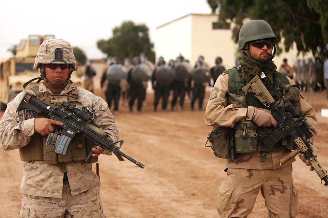 A U.S. Marine and Dutch soldier stand guard as a riot-control squad from Belgium moves into position behind them May 20 in the Tifnit, Morocco training area.  Crowd control was one of several demonstrations as general officers from participating countries observed what had been accomplished during the week-long training at the camp as a part of Exercise African Lion 2015. Exercise African Lion 15 is an annually-scheduled, combined U.S.–Moroccan exercise designed to improve mutual understanding of each nation’s tactics, techniques and procedures while demonstrating the strong bond between the two nation’s militaries.  The one-week exercise includes various types of military training, including a command post exercise; stability operations, such as nonlethal weapons training and crisis/disaster response training.  Additionally, in February an intelligence capacity building seminar was conducted.