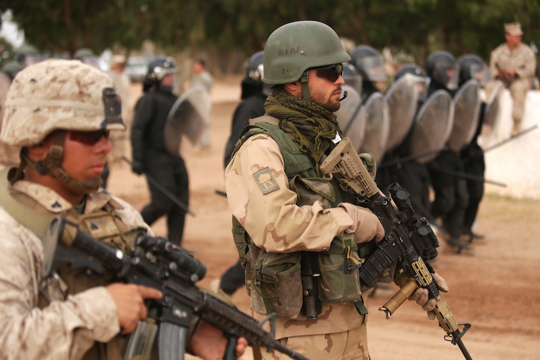 A U.S. Marine and Dutch soldier stand guard as a riot-control squad from Belgium moves into position behind them May 20 in the Tifnit, Morocco training area.  Crowd control was one of several demonstrations as general officers from participating countries observed what had been accomplished during the week-long training at the camp as a part of Exercise African Lion 2015. Exercise African Lion 15 is an annually-scheduled, combined U.S.–Moroccan exercise designed to improve mutual understanding of each nation’s tactics, techniques and procedures while demonstrating the strong bond between the two nation’s militaries.  The one-week exercise includes various types of military training, including a command post exercise; stability operations, such as nonlethal weapons training and crisis/disaster response training.  Additionally, in February an intelligence capacity building seminar was conducted.