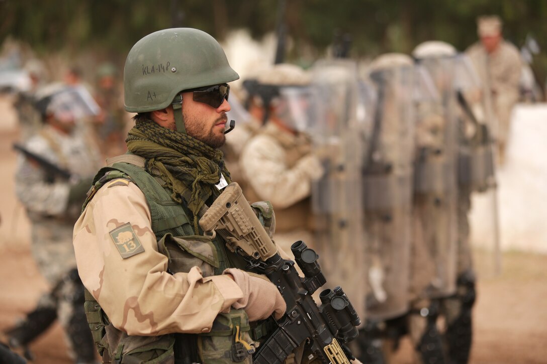 A Dutch soldier stands guard as a U.S. Marine Corps riot-control squad moves into position behind him May 20 in the Tifnit, Morocco training area.  Crowd control was one of several demonstrations as general officers from participating countries observed what had been accomplished during the week-long training at the camp as a part of Exercise African Lion 2015. Exercise African Lion 15 is an annually-scheduled, combined U.S.–Moroccan exercise designed to improve mutual understanding of each nation’s tactics, techniques and procedures while demonstrating the strong bond between the two nation’s militaries.  The one-wee exercise includes various types of military training, including a command post exercise; stability operations, such as nonlethal weapons training and crisis/disaster response training.  Additionally, in February an intelligence capacity building seminar was conducted.