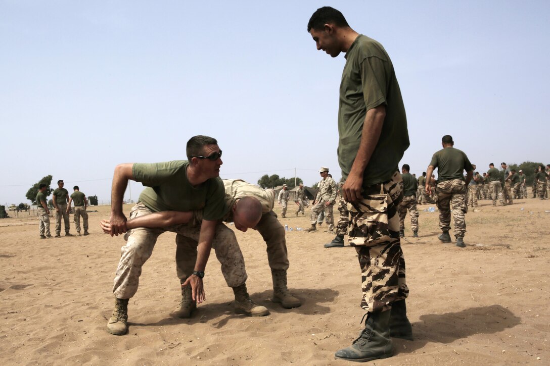 U.S. Marine Corps Staff Sgt. Kevin Morrow, 2nd Law Enforcement Battalion, and a Belgian soldier show nonlethal-combative techniques to a Royal Moroccan Armed Forces soldier during Exercise African Lion 15, May 15, in Tifnit, Morocco. Service members from the Moroccan, U.S., U.K., Belgian, and Netherland Armed Forces were completely integrated as one unit to improve military capabilities while working as an international coalition during the exercise.