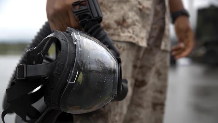 A Marine holds his gas mask after completing leak, seal, package and decontamination training April 21 at the gas chamber on Camp Hansen, Okinawa. Explosive ordnance disposal technicians and chemical, biological, radiological, nuclear defense specialists placed a leaking ordnance package in the gas chamber, using chlorobenzylidene malonitrile, also known as tear gas, to simulate the emission of harmful gases. The EOD technicians and CBRN defense specialists used protective equipment to perform general decontamination of the affected area and prepare the leaking ordnance for safe containment and transport before completing the decontamination process. 