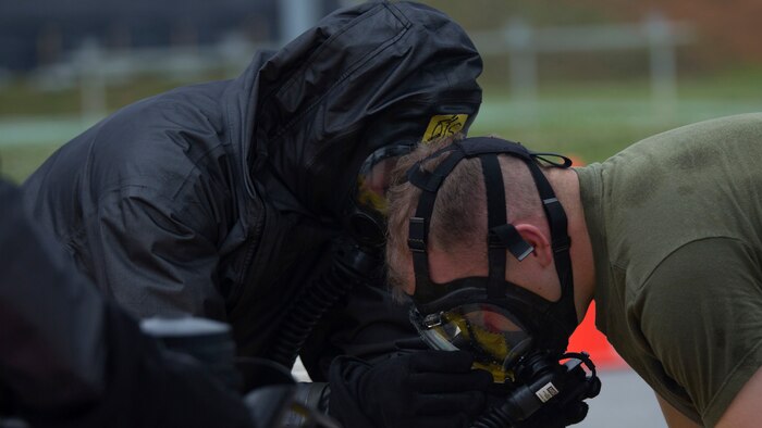 A chemical, biological, radiological, nuclear defense specialist assists a Marine in removing his gas mask after leak, seal, package and decontamination training April 21 at the gas chamber on Camp Hansen, Okinawa. Explosive ordnance disposal technicians and chemical, biological, radiological, nuclear defense specialists placed a leaking ordnance package in the gas chamber, using chlorobenzylidene malonitrile, also known as tear gas, to simulate the emission of harmful gases. The EOD technicians and CBRN defense specialists used protective equipment to perform general decontamination of the affected area and prepare the leaking ordnance for safe containment and transport before completing the decontamination process.