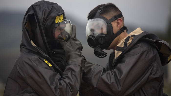 Two chemical, biological, radiological, nuclear defense specialists ensure gas masks are properly fitted prior to leak, seal, package and decontamination training April 21 at the gas chamber on Camp Hansen, Okinawa. The CBRN defense specialists assisted in familiarizing explosive ordnance disposal technicians with decontamination procedures following the leak, seal, package process used to mitigate CBRN-related hazards.