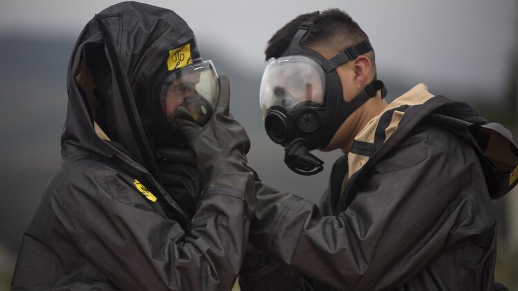 Two chemical, biological, radiological, nuclear defense specialists ensure gas masks are properly fitted prior to leak, seal, package and decontamination training April 21 at the gas chamber on Camp Hansen, Okinawa. The CBRN defense specialists assisted in familiarizing explosive ordnance disposal technicians with decontamination procedures following the leak, seal, package process used to mitigate CBRN-related hazards.