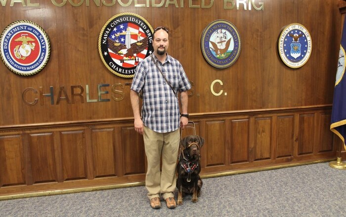 Stephen Hart, a U.S. Army veteran poses with Baara, a two and-a-half year old chocolate Labrador mix following a dog placement ceremony May 21, 2015 at the Naval Consolidated Brig Charleston on Joint Base Charleston, S.C.  Baara was trained by inmates at the NCBC in partnership with Canines For Service, Inc. Canines for Service is a national program that provides disabled veterans with quality, trained service dogs. The program teams military prisoners at the NCBC with future service dogs,  many that have been rescued from local animal shelters. Baara arrived for training at NCBC May 29, 2014 from the Doc Williams SPCA in Monck's Corner, S.C., and will assist Hart with both his mobility and posttraumatic stress disorder commands. Hart is excited to welcome Baara into his life and hopes he will help bring about a sense of normalcy to his life. (NCBC courtesy photo) 