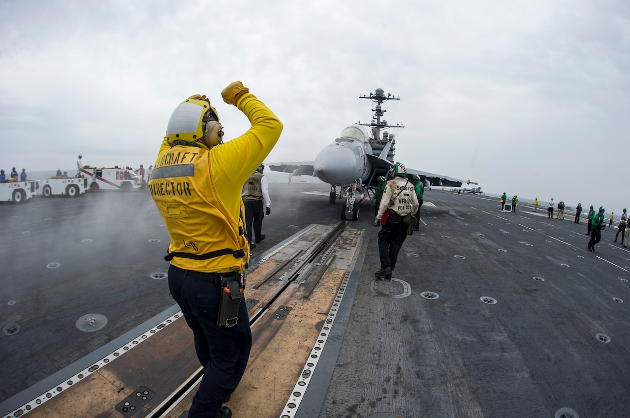 Navy Petty Officer 2nd Class Chris Gibson, left, an aviation boatswain's mate (handling), signals to the pilot of an F/A-18F Super Hornet assigned to Strike Fighter Squadron 102 on the flight deck of the aircraft carrier USS George Washington, May 19, 2015. U.S. Navy photo by Seaman Bryan Ma