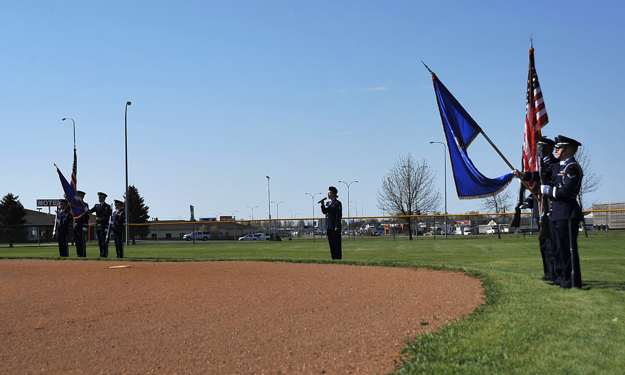 Honor Guards from Grand Forks and Minot Air Force Bases present the colors while Staff Sgt. Heather Veldhouse from Minot’s 5th Munitions Squadron sings the national anthem to signify the beginning of the softball tournament between the two bases at Roosevelt Park in Devils Lake, N.D., May 21, 15. The tournament was the first time the two bases came together on the field of play for a morale boosting event. (U.S. Air Force photo by Airman 1st Class Bonnie Grantham/Released)