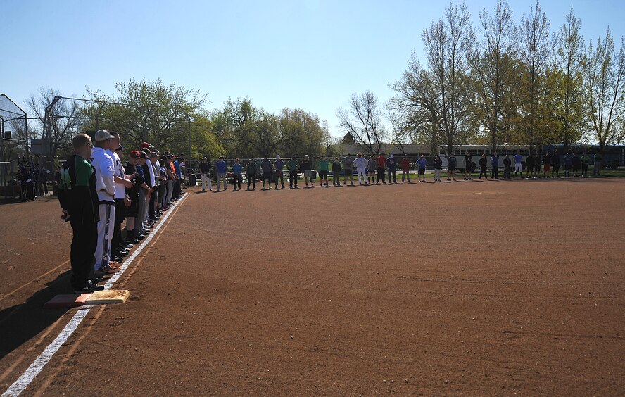Airmen from Grand Forks and Minot Air Force Bases line up along the baseline of the baseball field as the Grand Forks AFB and Minot AFB Honor Guards prepare to enter the field to present the colors during the singing of the national anthem at Roosevelt Park in Devils Lake, N.D., May 21, 15. The tournament was the first time the two bases came together on the field of play for a morale boosting event. (U.S. Air Force photo by Airman 1st Class Bonnie Grantham/Released)