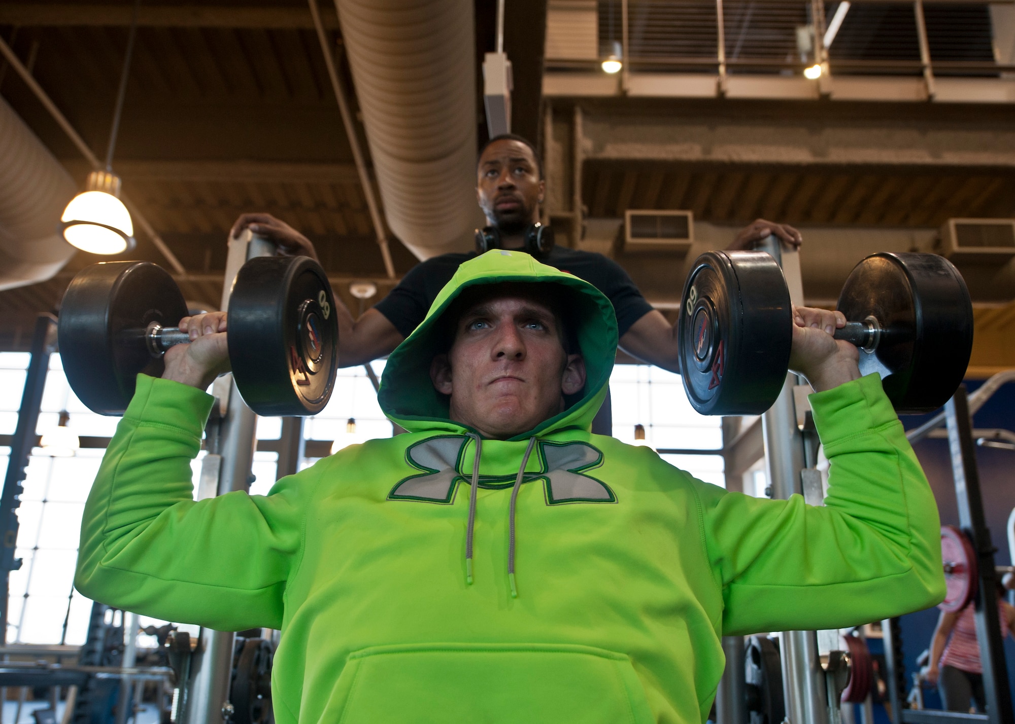 Senior Airman Vincent Costante, 99th Logistics Readiness Squadron fuels laboratory technician, performs a shoulder dumb bell press with the assistance of his trainer, Staff Sgt. Travis Mitchell, 99th LRS NCO in charge of fuels preventive maintenance, at the Warrior Fitness Center on Nellis Air Force Base, Nev., May 26, 2015. Costante wants to one day be a professional bodybuilder with the hopes of becoming Mr. Olympia. (U.S. Air Force photo by Airman 1st Class Jake Carter)