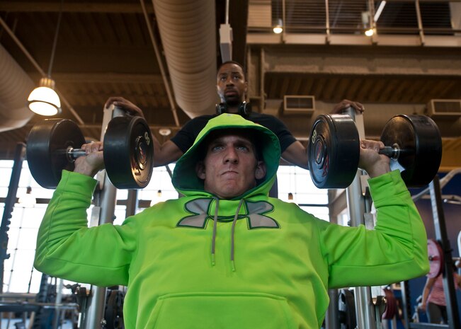 Senior Airman Vincent Costante, 99th Logistics Readiness Squadron fuels laboratory technician, performs a shoulder dumb bell press with the assistance of his trainer, Staff Sgt. Travis Mitchell, 99th LRS NCO in charge of fuels preventive maintenance, at the Warrior Fitness Center on Nellis Air Force Base, Nev., May 26, 2015. Costante wants to one day be a professional bodybuilder with the hopes of becoming Mr. Olympia. (U.S. Air Force photo by Airman 1st Class Jake Carter)