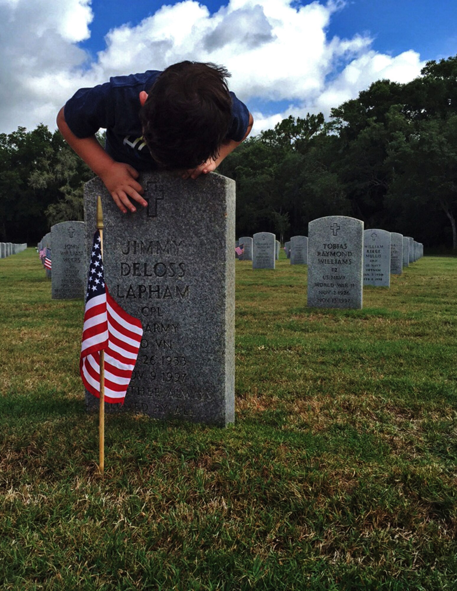 A young boy traces the cross engraved on his great grandfather’s headstone at Florida National Cemetery in Bushnell, Fla., May 24, 2015. Hundreds of volunteers placed American flags in front of more than 300 acres of headstones belonging to military veterans. (U.S. Air Force photo by Senior Airman Bulow-Gonterman/Released)  
