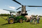 Members of Companies B and C, 2nd Battalion, 149th General Aviation Support Battalion, Oklahoma Army National Guard, and local farm and ranch hands from Muskogee County load a 1,200-pound round bale of hay aboard a CH-47 Chinook helicopter. The Chinook's crew delivered a total of 14 bales weighing more than 14,000 pounds and 700 pounds of feed to the stranded cattle.