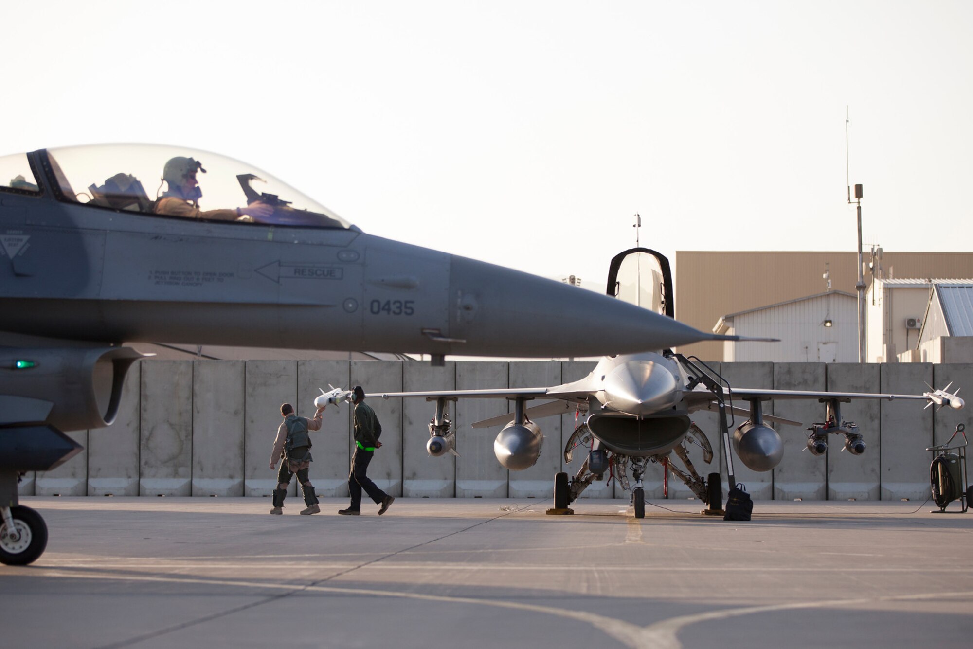 A U.S. Air Force F-16 Fighting Falcon pilot assigned to the 555th Expeditionary Fighter Squadron taxies to de-arm after flying a combat sortie as Airman 1st Class John Reid, 455th Expeditionary Aircraft Maintenance Squadron assistant dedicated crew chief, accompanies another pilot during his preflight walk at Bagram Airfield, Afghanistan, Aug. 31, 2015. The F-16 is a multi-role fighter aircraft that is highly maneuverable and has proven itself in air-to-air and air-to-ground combat.  (U.S. Air Force photo by Master Sgt. Kevin Crawford/Released)