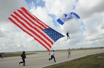 A member of the U.S. Air Force Wings of Blue parachute team carries the U.S. national flag, as volunteers prepare to catch it during the 2015 Joint Base San Antonio Air Show and Open House Nov. 1, 2015 at Joint Base San Antonio-Randolph, Texas. Air shows allow the Air Force to display the capabilities of our aircraft to the American taxpayer through aerial demonstrations and static displays and allowing attendees to get up close and personal to see some of the equipment and aircraft used by the U.S. military today. (U.S. Air Force photo by Melissa Peterson) 