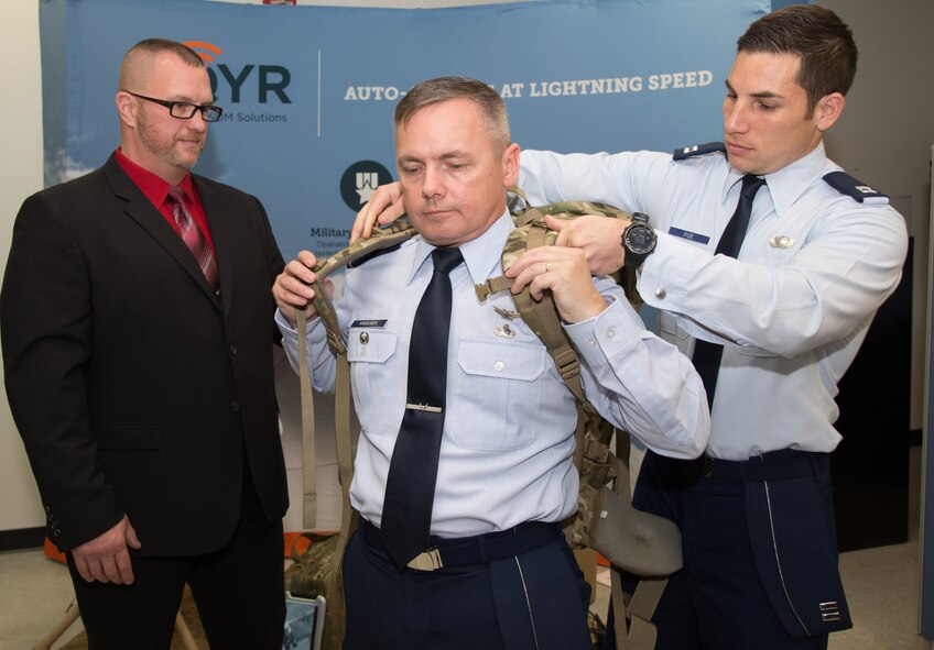 Capt. Hayden Poe, far right, a Global Broadcast Service program manager, fastens a GBS rucksack-portable receive suite device onto Col. Todd Krueger, Space, Aerial and Nuclear Networks senior materiel leader, Oct. 30, 2015. AQYR Technologies was recently awarded Hanscom Air Force Base's largest small business innovation research contract to date for the production and delivery of the devices. The receive devices come in a suitcase- and rucksack-portable size that will allow service members to receive near real-time video and data in remote locations. (U.S. Air Force photo/Mark Herlihy)