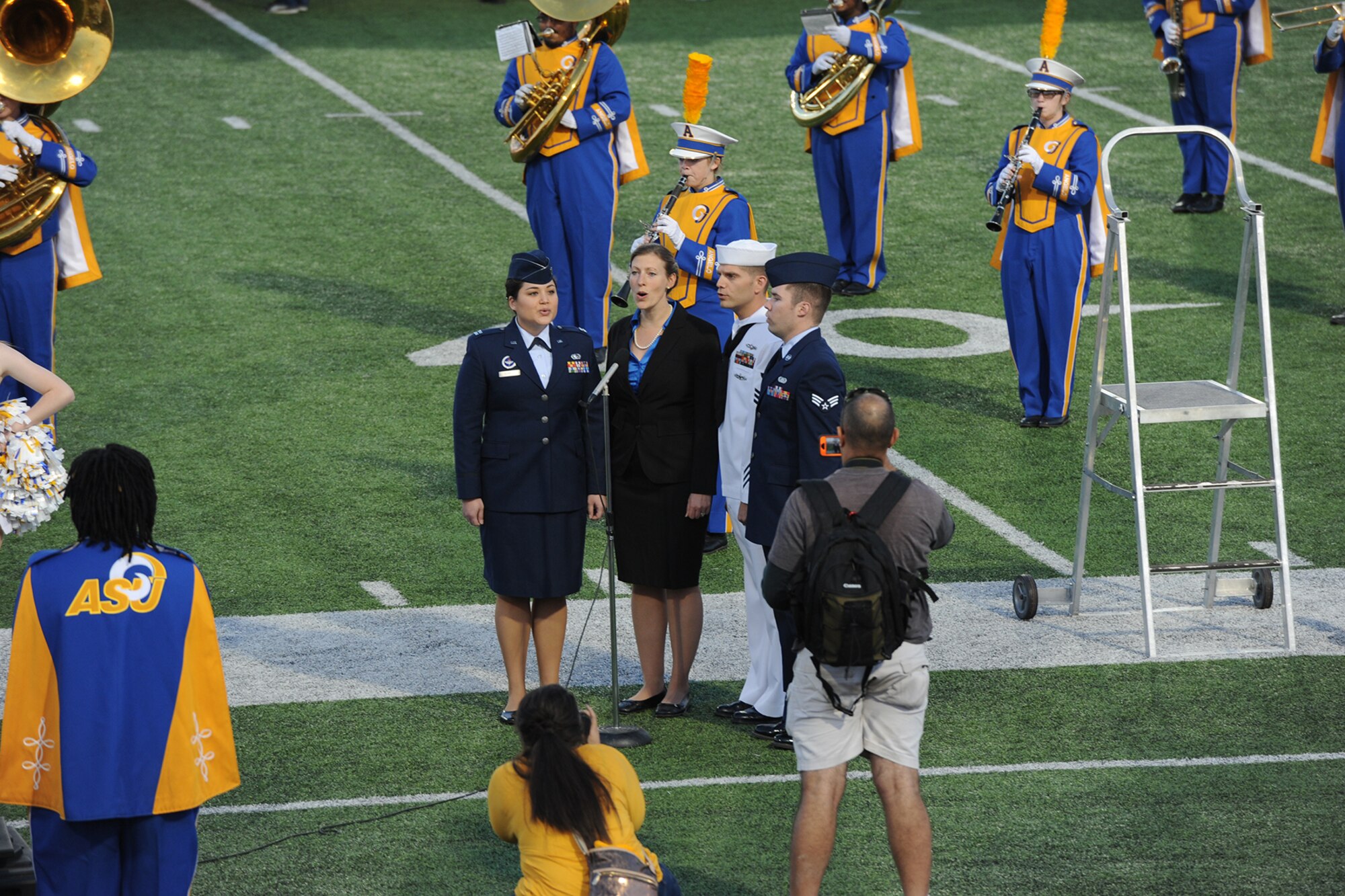 Patriotic Blue sings the national anthem as the Angelo State University marching band performs during the opening ceremony of ASU’s Military Appreciation Day football game at the LeGrand Stadium, San Angelo, Texas, Oct. 31, 2015. Patriotic Blue is a singing group of comprised of service members and civilians from Goodfellow Air Force Base. (U.S. Air Force photo by Staff Sgt. Laura R. McFarlane/Released)