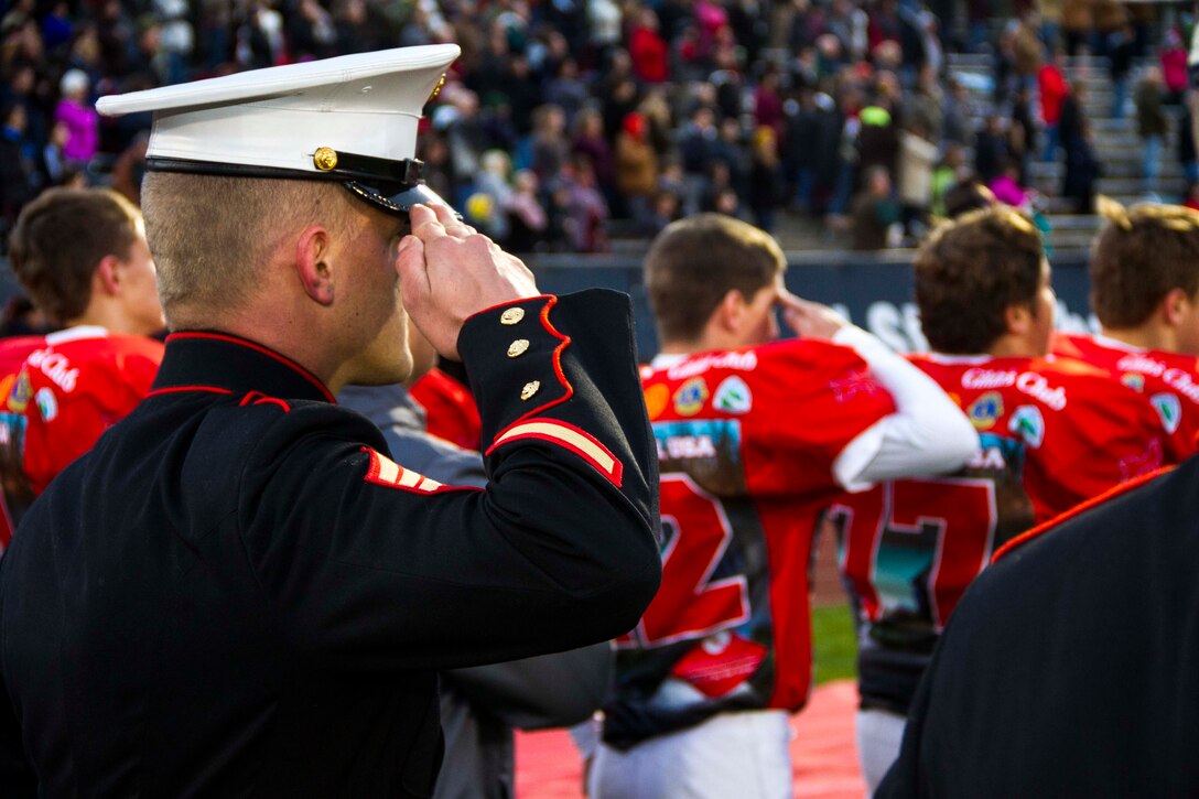 Sgt. Matthew Boulis, recruiter with Recruiting Sub Station Grand Rapids North, Mich., and a football player from Lowell High School, salute the flag during the National Anthem  before the start of the Great American Rivalry Series game between Lowell and East Grand Rapids high schools, Oct. 16, 2015. The Great American Rivalry Series games allowed Marines, football players and the school’s student body to interact over a relatable common ground topic: competition. 