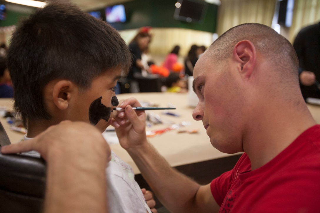 Sergeant Chance Love, from Sturgis, South Dakota, paints a “bat symbol” on 11-year-old Yoshihama Ryuga’s face at the Trunk-or-Treat event on Camp Schwab, Okinawa, Japan, on Oct. 31. This was the first year a Halloween event was held on base for the members of the Henoko community. There was food, candy and face painting at the event. U.S. Marines are good neighbors who are engaged with and contribute to Okinawa communities. Love is a field radio operator with 3rd Reconnaissance Battalion, 3rd Marine Division, III Marine Expeditionary Force.
