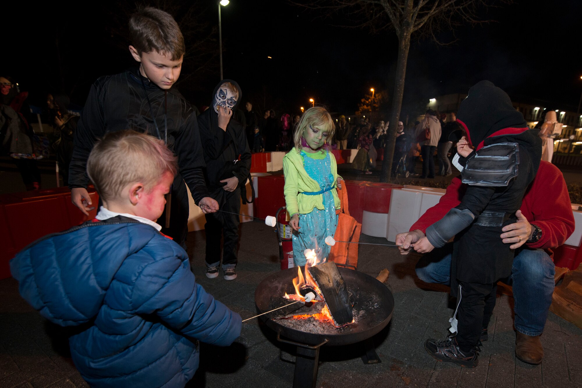 Trick-or-treaters and their family members roast marshmallows for smores during Family Fright Night at the Club Eifel parking lot on Spangdahlem Air Base, Germany, Oct. 30, 2015. More than 400 people attended the Halloween block party, hosted by the 52nd Force Support Squadron. (U.S. Air Force photo by Staff Sgt. Christopher Ruano/Released)