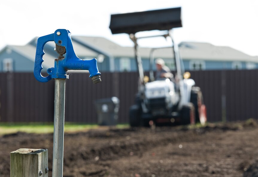 A water spigot stands ready to use at the new 60-foot by 120-foot organic community garden Oct. 29, 2015, on Dover Air Force Base, Del. John Clendaniel, Delaware State University College of Agriculture and Related Sciences farm management specialist, in the background, tilled the leaf mulch into the soil with equipment belonging to the DSU College of Agriculture and Related Sciences small farms department, one of many Air Force Community Partnership Program P4 initiative stakeholders. (U.S. Air Force photo/Roland Balik)