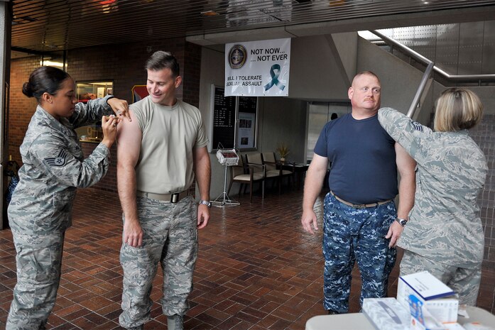 (left) Staff Sgt. Talisa Bell and (right) Staff Sgt. Abigail Johannesson, 628th Medical Operations Squadron immunizations technicians, vaccinate Chief Master Sgt. Mark Bronson, 628th Air Base Wing command chief and Command Master Chief Joseph Gardner at the headquarters building on Joint Base Charleston - Air Base, S.C., Nov. 3, 2015. Receiving an annual flu shot satisfies this component of their Individual Mobility Readiness requirements.(U.S. Air Force photo/Tech. Sgt. Renae Pittman)