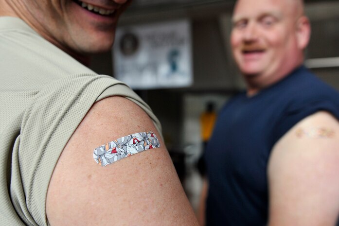(left) Chief Master Sgt. Mark Bronson, 628th Air Base Wing command chief and Command Master Chief Joseph Gardner show off their Looney Toons band aids after receiving the flu vaccination at Joint Base Charleston, S.C., Nov. 3, 2015. (U.S. Air Force photo/Tech. Sgt. Renae Pittman)
