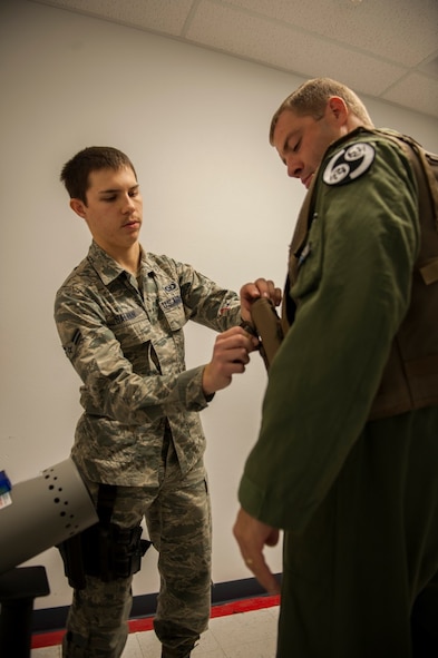 Airman 1st Class Austin Galvan, 5th Operations Support Squadron aircrew flight equipment apprentice, helps a pilot holster his weapon at Minot Air Force Base, N.D., Oct. 30, 2015. AFE helps to train pilots prior to upcoming exercises for safety. (U.S. Air Force photo/Airman 1st Class Christian Sullivan)