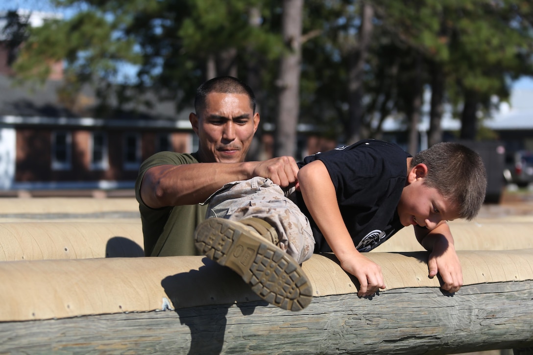 Sgt. Amado Benin aids D’Angelo, 10, through an obstacle during the Marine Wing Headquarters Squadron 2’s Warrior Day at Marine Corps Air Station Cherry Point, N.C., Oct.30, 2015. Marines with MWHS-2 hosted an interactive day where families could participate in some of the routine training Marines undergo. Family members had the opportunity to fire in a simulated range, experience night vision equipment, partake in a Combat Fitness Test, receive a Marine Corps Martial Arts Program class and brave the obstacle course. Benin is an imagery analysis specialist with MWHS-2 and D’Angelo is the brother of Cpl. Raquel Mathieu, an intelligence specialist with the squadron. (U.S. Marine Corps photo by Cpl. N.W. Huertas/ Released)