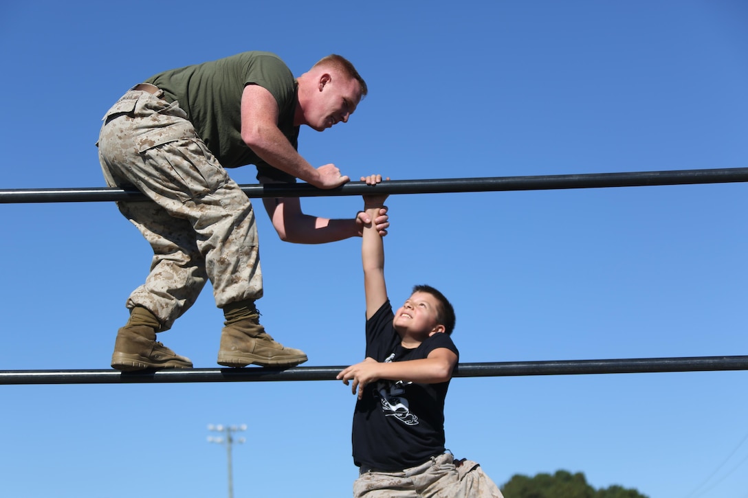 Sgt. Joshua Kessinger aids D’Angelo, 10, over an obstacle during the Marine Wing Headquarters Squadron 2’s Warrior Day at Marine Corps Air Station Cherry Point, N.C., Oct.30, 2015. Marines with MWHS-2 hosted an interactive day where families could participate in some of the routine training Marines undergo. Marines use obstacle courses as part of their routine physical exercise as it tests their physical endurance and teamwork. Kessinger is a Chemical, biological, radiological, nuclear specialist and D’Angelo is the brother of Cpl. Raquel Mathieu, and intelligence specialist, both with the squadron. (U.S. Marine Corps photo by Cpl. N.W. Huertas/ Released)