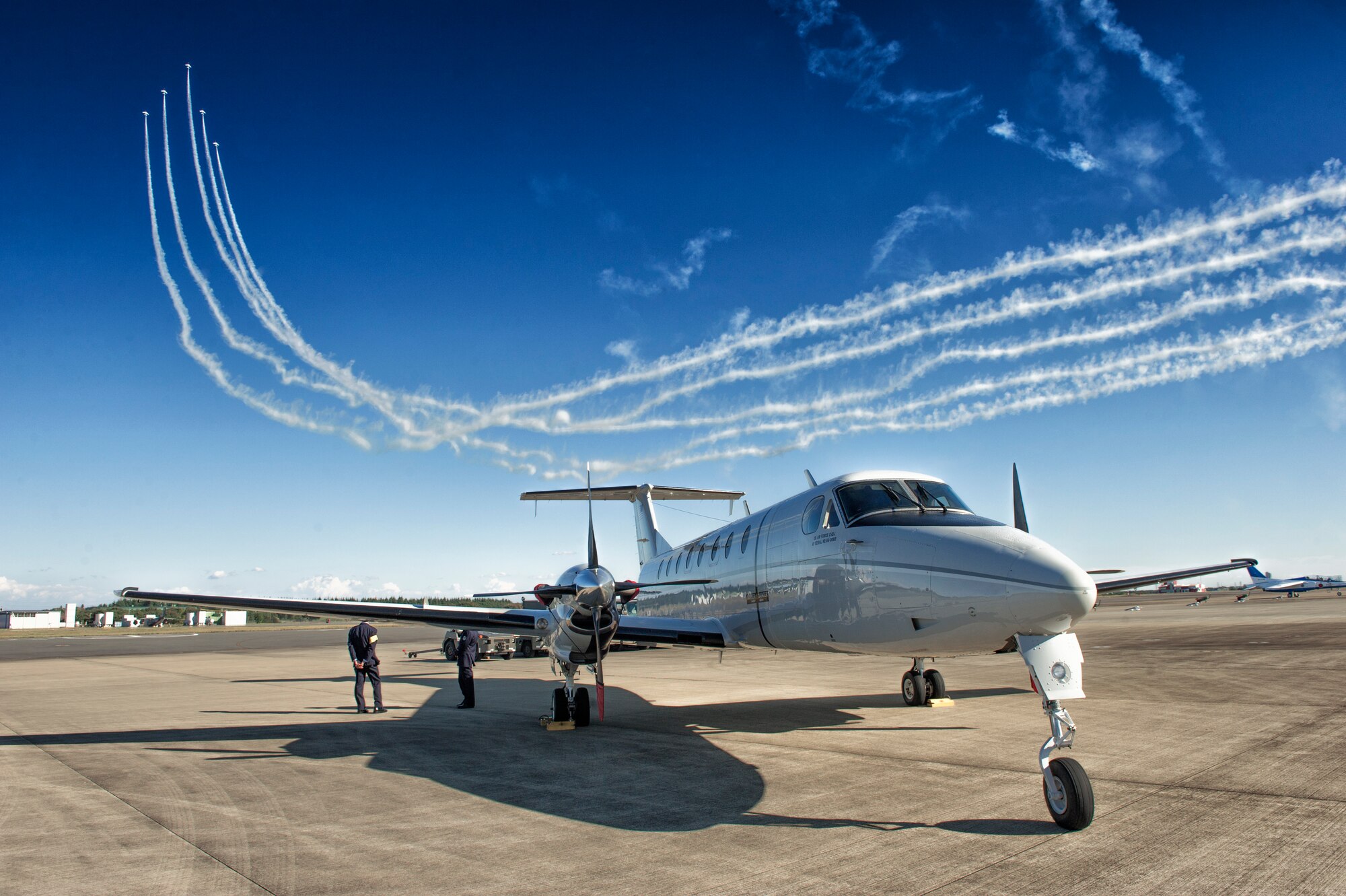 The Japan Air Self-Defense Force aerobatic team, Blue Impulse, leaves smoke-trails in the sky over a Yokota C-12 Huron during an air show at Iruma Air Base, Japan, Nov. 3, 2015. This year marked the second time Yokota aircraft were featured in the Iruma Air Show. (U.S. Air Force photo by Airman 1st Class Delano Scott/Released) 