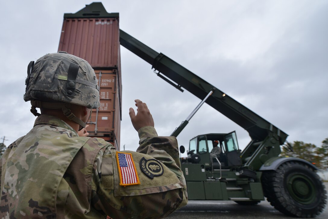 U.S. Army Spc. Brandon Dominguez, Maritime and Intermodal Training School student, directs Pfc. Richard Jones, Maritime and Intermodal Training School student, during the rough terrain container handler course at Fort Eustis, Va., Oct. 28, 2015. The program teaches experienced Soldiers enhanced cargo loading and operating skills.  (U.S. Air Force photo by Staff Sgt. Natasha Stannard/ Released)
