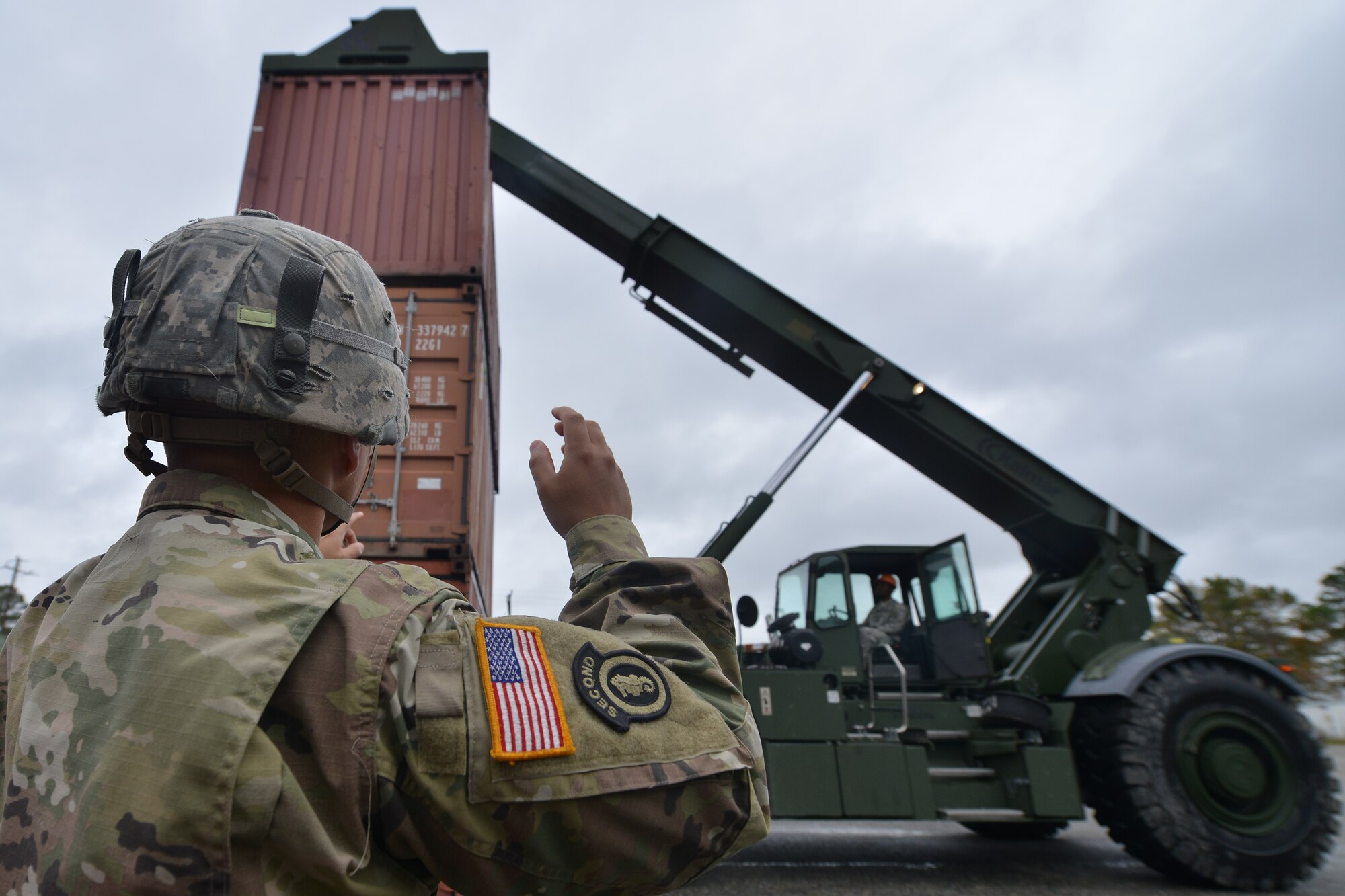 U.S. Army Spc. Brandon Dominguez, Maritime and Intermodal Training School student, directs Pfc. Richard Jones, Maritime and Intermodal Training School student, during the rough terrain container handler course at Fort Eustis, Va., Oct. 28, 2015. The program teaches experienced Soldiers enhanced cargo loading and operating skills.  (U.S. Air Force photo by Staff Sgt. Natasha Stannard/ Released)