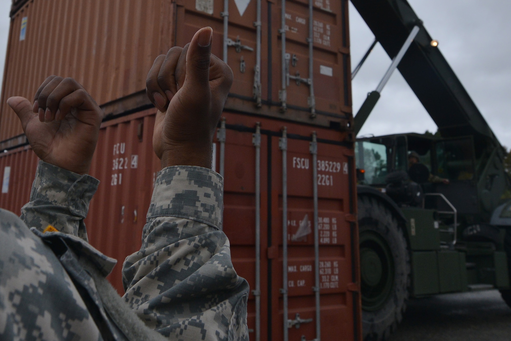 U.S. Army Pfc. Richard Jones, Maritime and Intermodal Training School student, guides a rough terrain container handler operator for the course at Fort Eustis, Va., Oct. 28, 2015. During the course, the students, who all hold various cargo specialties, learn how to direct and operate the handlers which can move 20 and 40 foot containers, carrying essential supplies. (U.S. Air Force photo by Staff Sgt. Natasha Stannard/ Released)