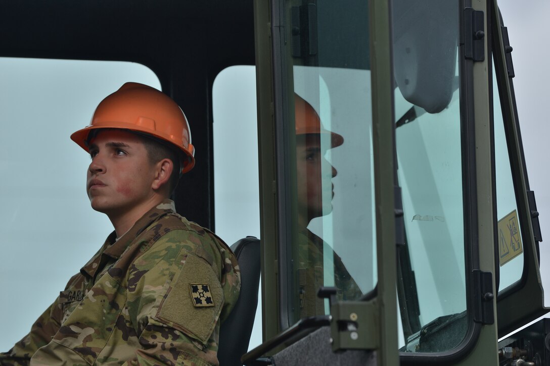 U.S. Army Pvt. Marcus Garcia, Maritime and Intermodal Training School student, looks to a student directing his container handler movements at Fort Eustis, Va., Oct. 28, 2015. Throughout the rough terrain container handler course, operators are paired with directors to ensure the cargo is properly stacked. (U.S. Air Force photo by Staff Sgt. Natasha Stannard/ Released)