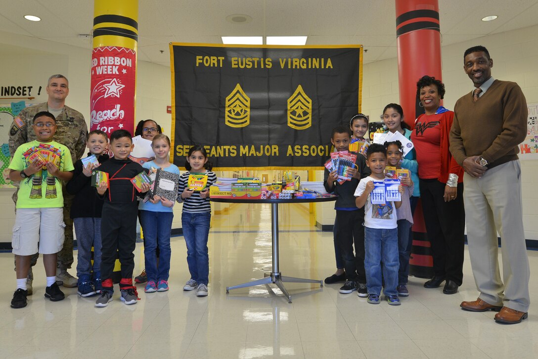 The Eustis Sergeants Major Association stands with General Stanford Elementary School students and faculty by a table of donated school supplies at Fort Eustis, Va., Oct. 30, 2015. Each year, the association teams up with the school to prioritize, collect and donate items that enable students to complete required school projects throughout the year. (U.S. Air Force photo by Staff Sgt. Natasha Stannard/Released)