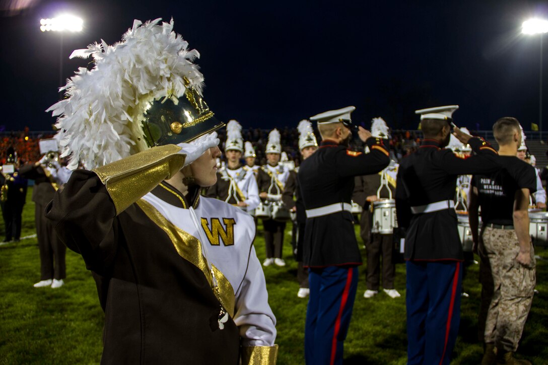 A Drum Major from Bay City Western High School, Staff Sgt. Luke DeJong and Sgt. Christopher Parker from Recruiting Sub Station Saginaw, Mich., salute the flag during the National Anthem before the start of the Great American Rivalry Series game between Bay City Central and Bay City Western high schools, Oct. 23, 2015.