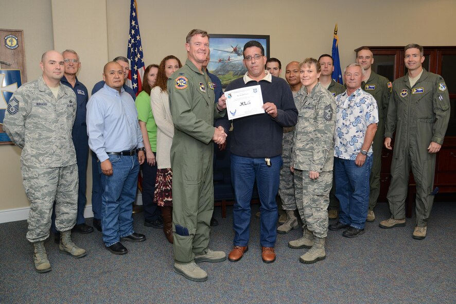 Joseph Pagan, center, 47th Operations Group quality assurance chief and building custodian, poses with Col. Thomas Shank, 47th Flying Training Wing commander, Chief Master Sgt. Teresa Clapper, 47th FTW command chief, after accepting the “XLer of the Week” award, here, Nov. 4, 2015. The “XLer” is a weekly award chosen by wing leadership and is presented to those who consistently make outstanding contributions to their unit and Laughlin. (U.S. Air Force photo by Airman 1st Class Ariel D. Partlow) (Released)