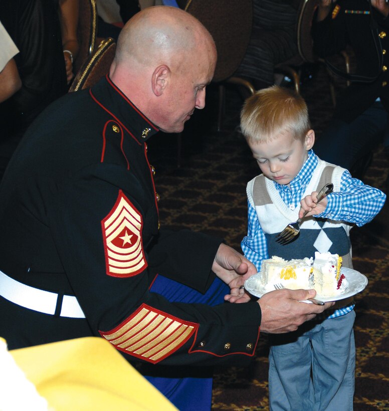 Sgt. Maj. Joseph M. Davenport, sergeant major, Marine Corps Logistics Command, the oldest Marine present at the Kids' Marine Corps Birthday Ball at Marine Corps Logistics Base Albany, passes a slice of cake to the youngest child, Louis Mixa, 2, during a cake-cutting ceremony, Nov. 3. Louis Mixa is the son of Maj. Matthew Mixa, action officer, MCLC. About 150 people attended the first-time event at the Town and Country Restaurant's Grand Ballroom.