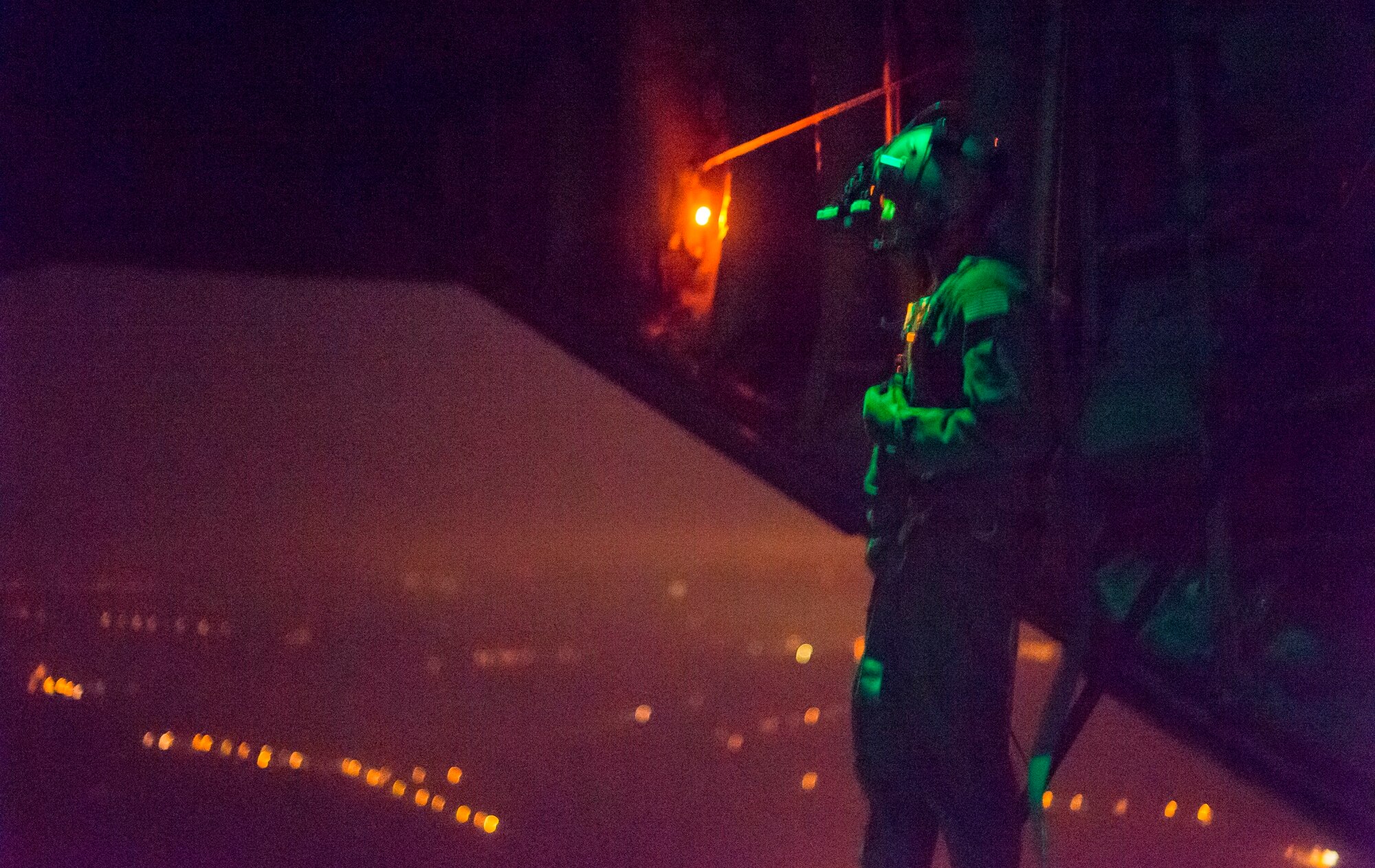 A U.S. Air Force 37th Airlift Squadron loadmaster looks out the back of a C-130J Super Hercules, Oct. 30, 2015, above Powidz Air Base, Poland. Loadmasters must train at night to familiarize themselves to the aircraft in low-light situations. (U.S. Air Force photo/Senior Airman Damon Kasberg)