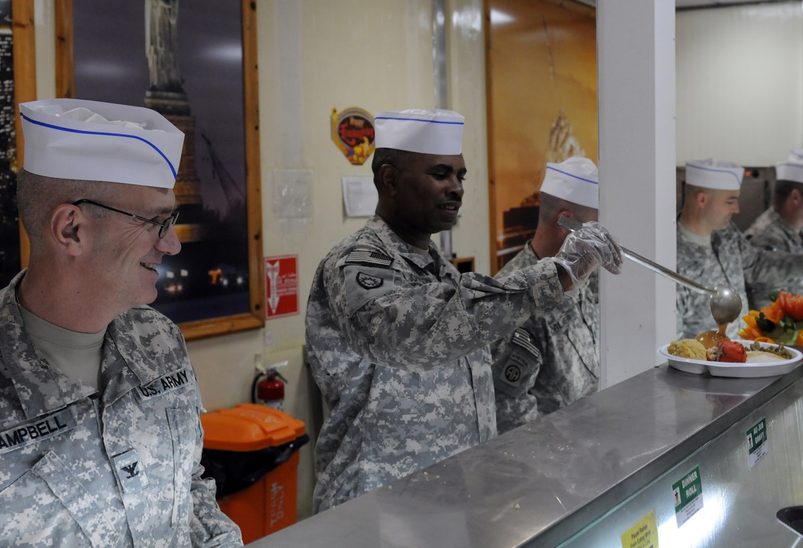 Army Command Sgt. Maj. Thomas Johnson of the Kentucky National Guard's 149th Maneuver Enhancement Brigade pours gravy on the plate of a Soldier as Army Col. Scott Campbell, 149th MEB commander, observes at Victory Base Complex, Iraq, on Nov. 20, 2011. The meal celebrated Thanksgiving for the remaining troops on VBC and was also the last hot meal served before the dining facility closed.